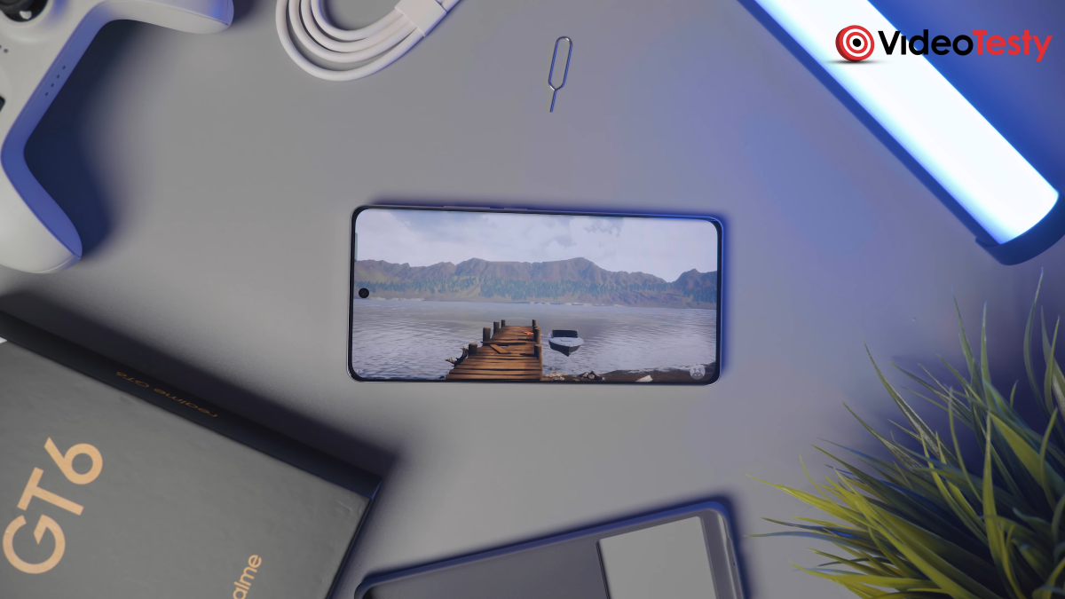 Realme GT 6 na szarym tle, wokół niego sporo rzeczy