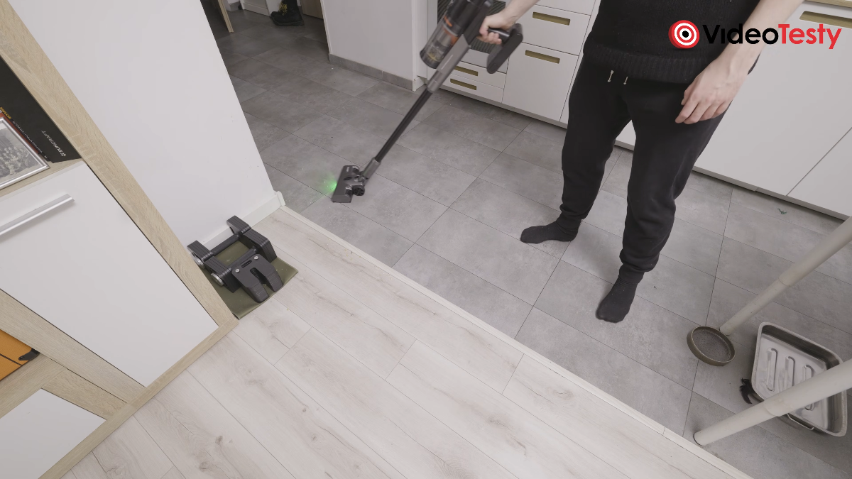 Mężczyzna odkurza w kuchni szarym odkurzaczem z zielonym podświetleniem