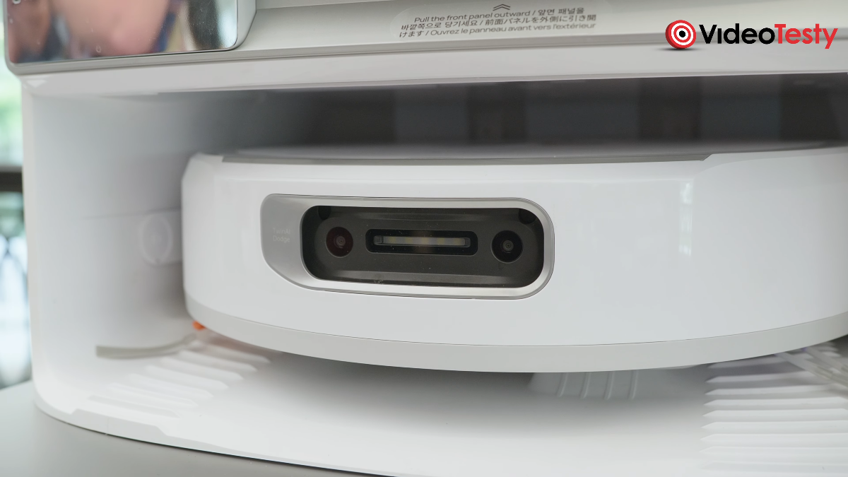 Biały robot w stacji, widziany od frontu. Ma czarną kamerę na przedzie