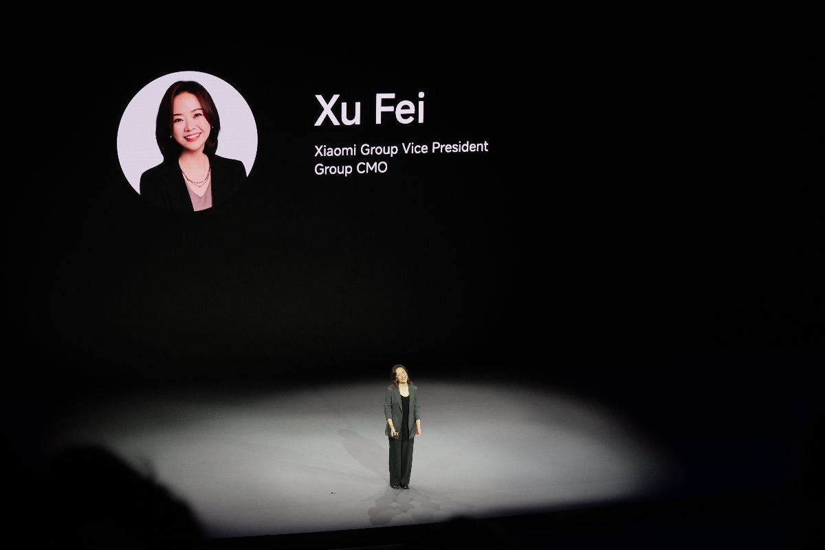 Kobieta na scenie podczas wydarzenia w Monachium. Tekst za nią: "Xu Fei, Xiaomi Group Vice President Group CMO"