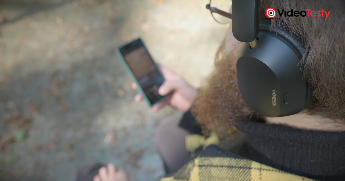 Brodaty mężczyzna wybiera muzykę na telefonie z czarnymi słuchawkami na uszach. Kadr zza pleców od góry