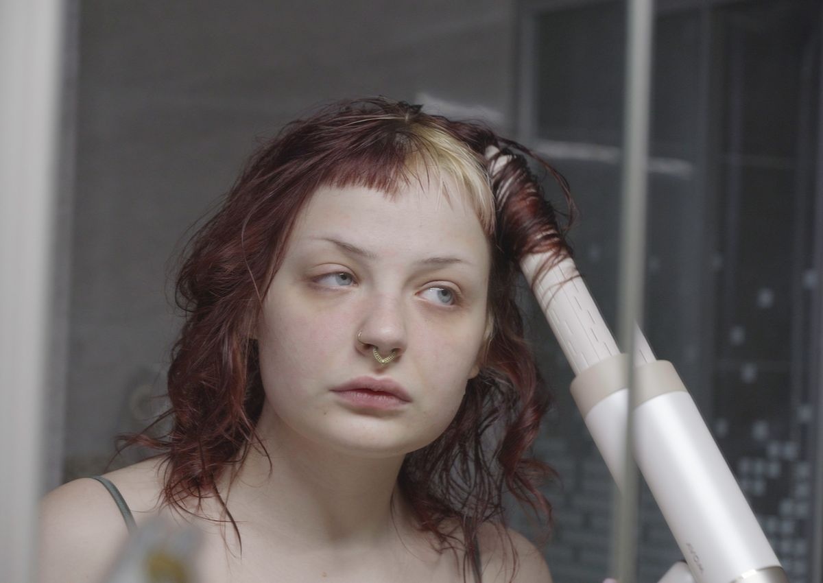 Kobieta korzysta z suszarki z funkcją lokówki. Kobieta ma czerwone włosy z blond akcentem