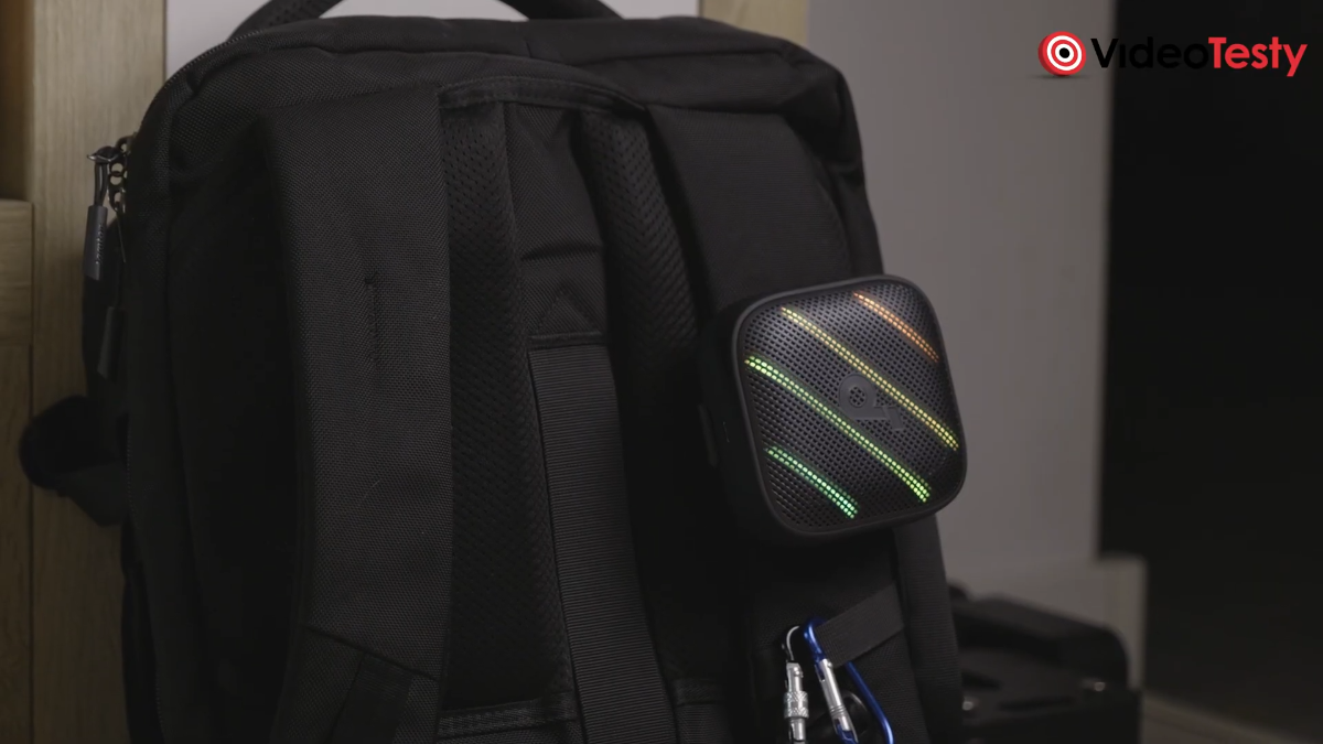 Soundcore Boom Go 3i, czarny głośnik z RGB przytroczony do czarnego plecaka na tle ściany
