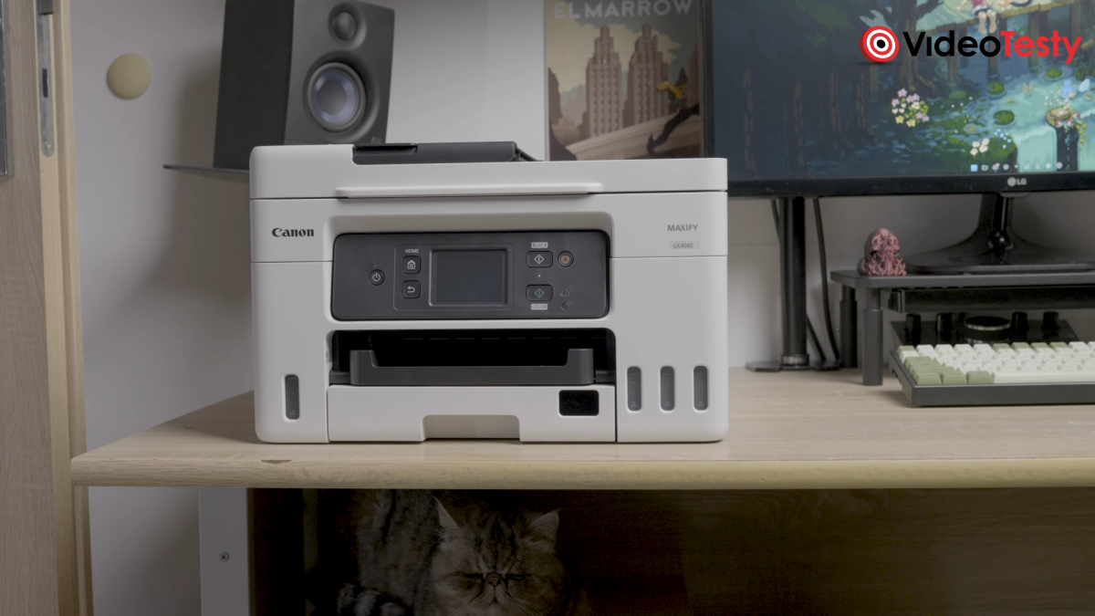Spojrzenie na drukarkę Canon MAXIFY GX4040 na biurku. Pod nią kryje się kot