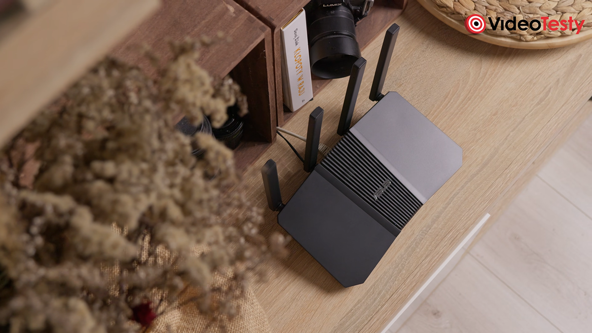 Widok od góry na czarny router znajdujący się na beżowym regale. Obok niego widać wysuszone zimowe rośliny