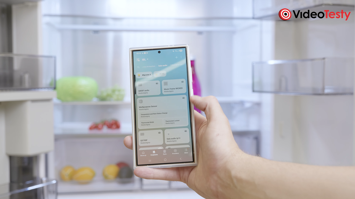 Mężczyzna korzysta na telefonie z AI Energy Mode. Za jego ręką widać lodówkę