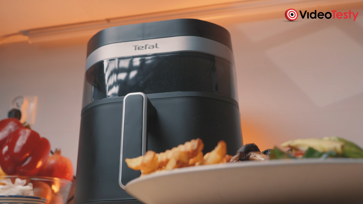 Czarna frytkownica z napisem tefal widziana od dołu, koło talerza z jedzeniem