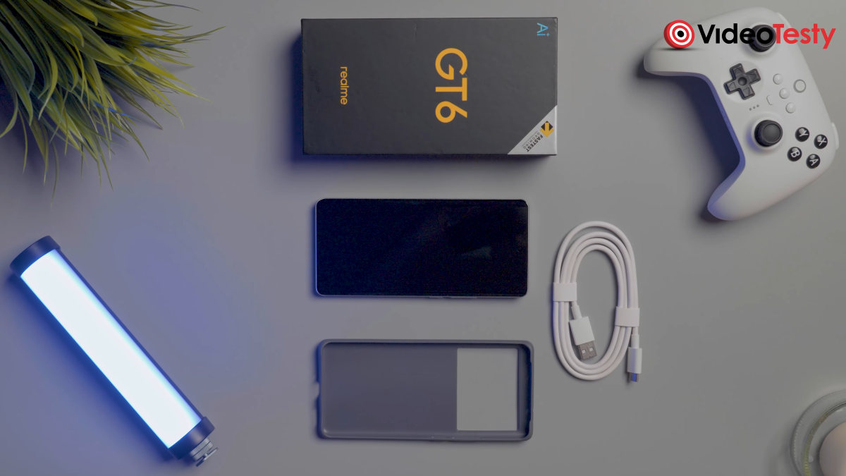Podstawowy zestaw Realme GT 6, na szarym tle widać między innymi pudełko, telefon, obudowę i kabel (oraz pada, światło i sztuczną roślinę, ale nie wchodzą w skład zestawu)