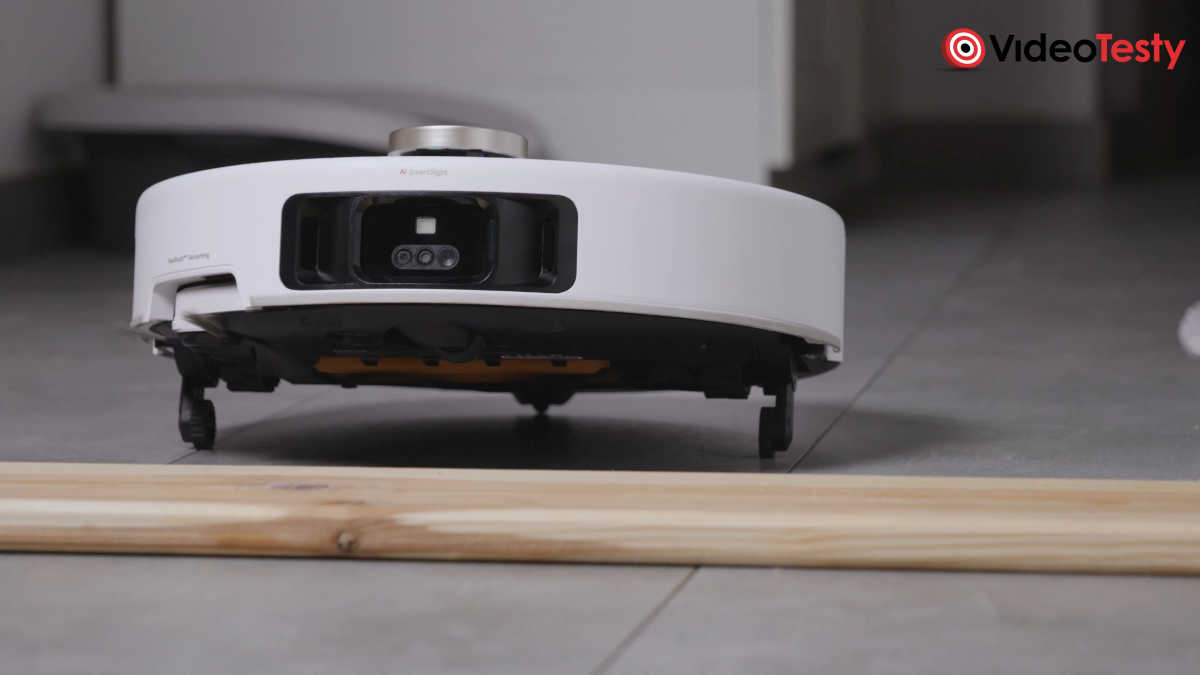 Biały robot z czarną kamerą na froncie podnosi się na czarnych kółkach do góry, aby wjechać na deskę