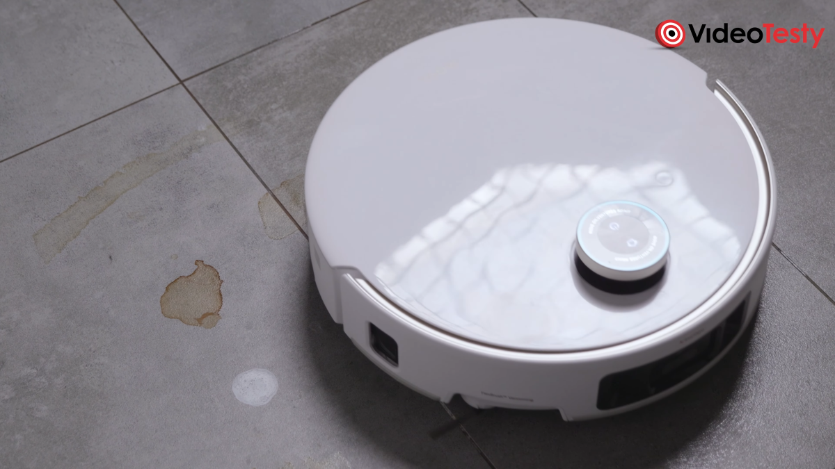 Robot podczas mopowania szarych kafelków. Znajduje się obok plamy po herbacie i paście do zębów