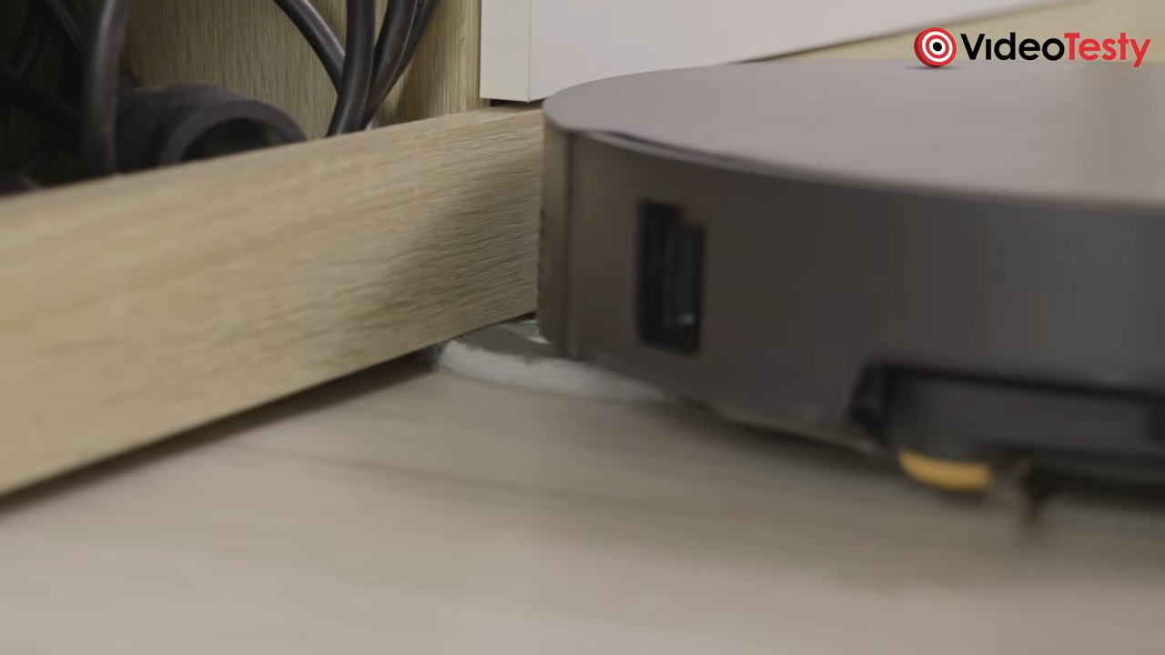 Czarny okrągły robot obraca się, aby doczyścić dyskiem podłogę pod meblami