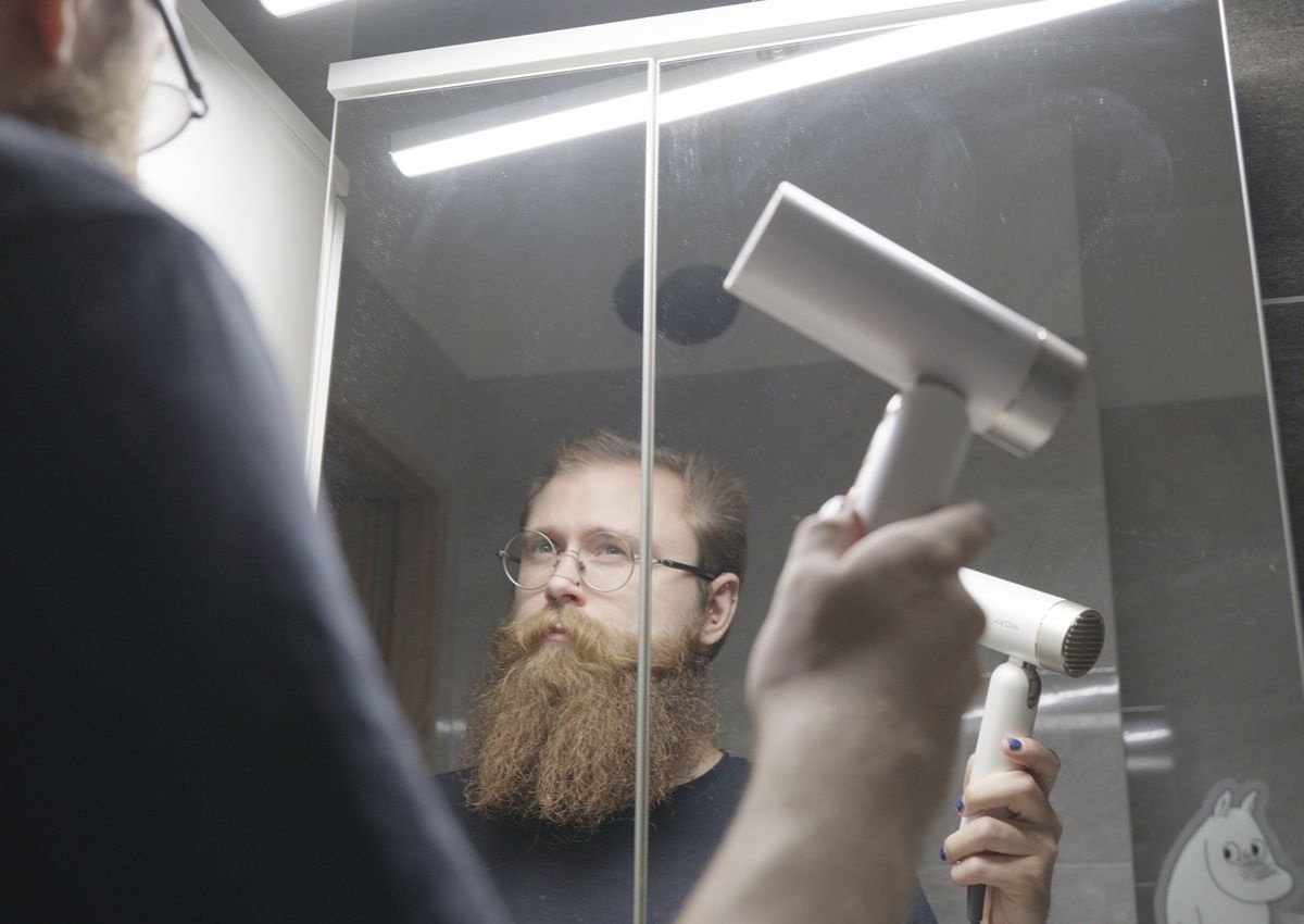 Mężczyzna suszy włosy białą suszarką w lustrze