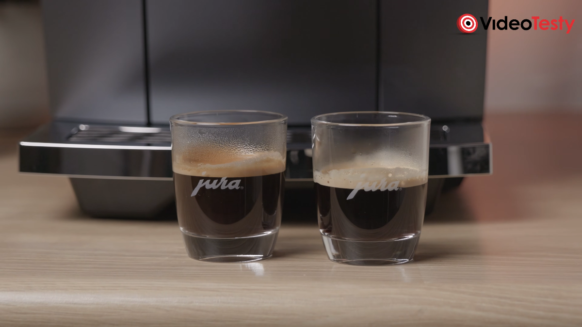 Dwie różne kawy espresso w szklankach przed czarnym ekspresem, na drewnianym blacie