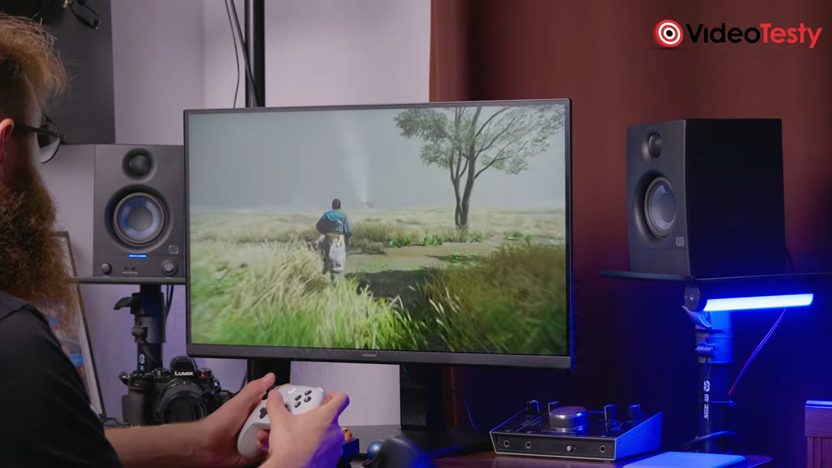Mężczyzna gra w Ghost of Tsushima na monitorze. Po prawej stronie widać głośnik z niebieskim podświetleniem na spodzie